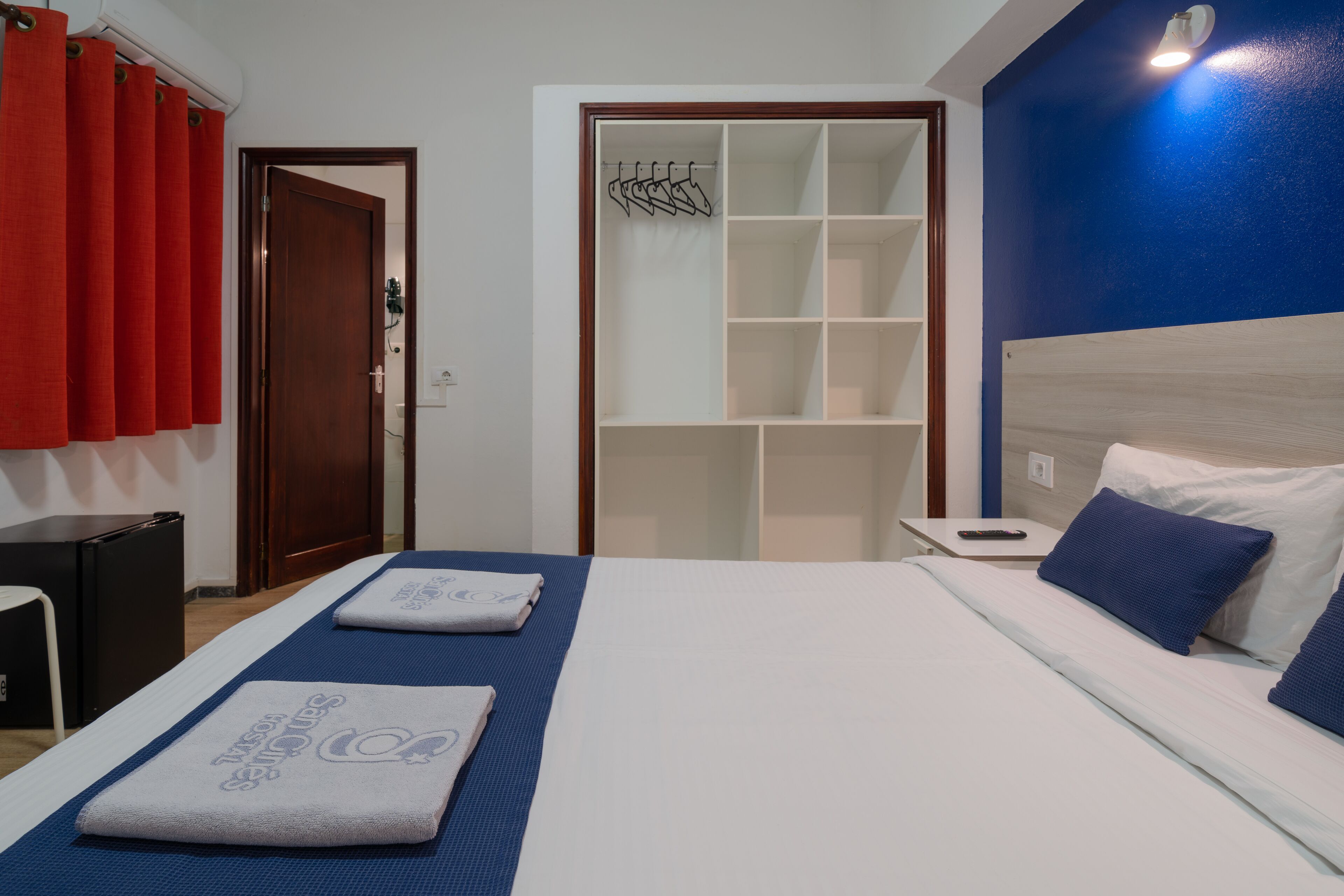 A hotel room with a bed, a nightstand, a wardrobe, and a red curtain.