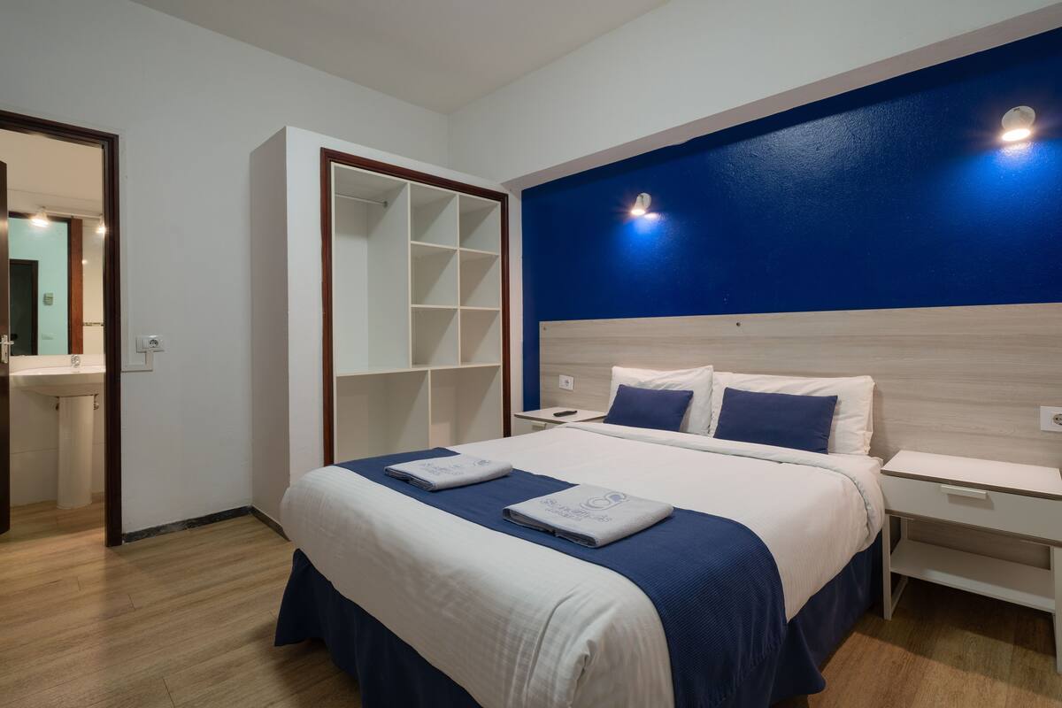 A modern hotel room with a large bed, a built-in wardrobe, a bedside table, and a nightstand.