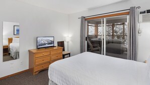 Une chambre d’hôtel avec un grand lit, une commode en bois, une télévision et une porte-fenêtre coulissante donnant sur un balcon avec vue sur des arbres couverts de neige.