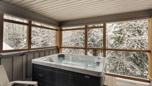 Un bain à remous installé sur une terrasse en bois, avec de grandes fenêtres donnant sur un paysage enneigé.