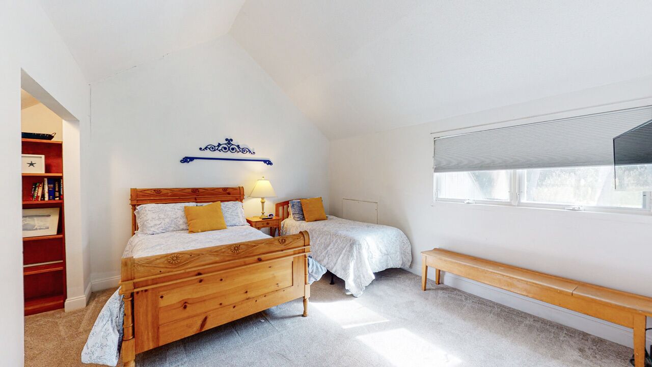 A bedroom with two wooden beds, a bookshelf, a bench, and a large window.