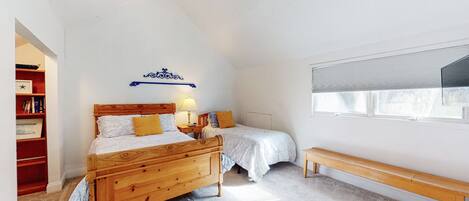 A bedroom with two wooden beds, a bookshelf, a bench, and a large window.
