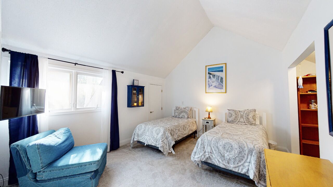Een slaapkamer met twee bedden, een stoel, een televisie en een boekenkast.