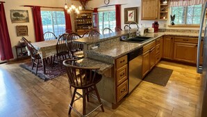 A spacious kitchen with wooden cabinets, a granite countertop, and a dining area with wooden chairs. - WaterfrontHome-Nature,Views,Peace-up to 12, ideal for Family/Friends/Celebration (Cambridge Springs)