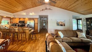 A spacious living area with a wooden ceiling, a dining area with wooden chairs, and a kitchen with modern appliances. - WaterfrontHome-Nature,Views,Peace-up to 12, ideal for Family/Friends/Celebration (Cambridge Springs)