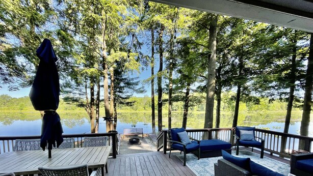 A wooden deck with outdoor furniture, a fire pit, and a view of a lake surrounded by trees. - WaterfrontHome-Nature,Views,Peace-up to 12, ideal for Family/Friends/Celebration (Cambridge Springs)