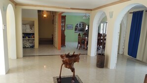A spacious living area with a dining table and chairs, a wooden sculpture, and a kitchen visible through an archway. - 5 Bed Room Villa with Swimming pool  (Montego Bay)