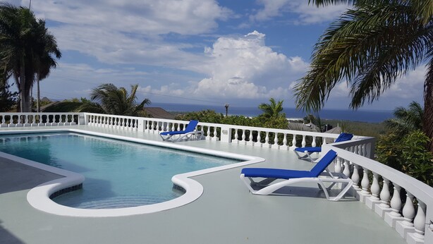 A swimming pool with blue lounge chairs and a white balustrade. - 5 Bed Room Villa with Swimming pool  (Montego Bay)