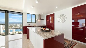 Una cocina moderna con una isla grande, armarios color rojo y vistas a la ciudad a través de amplias ventanas.