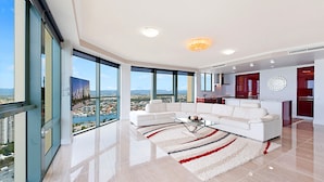 Un salón moderno con un sofá seccional blanco, una mesa de centro de vidrio y vista a un paisaje urbano a través de ventanas amplias.