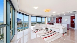 A modern living room with a white sectional sofa, a glass coffee table, and a view of a cityscape through large windows.