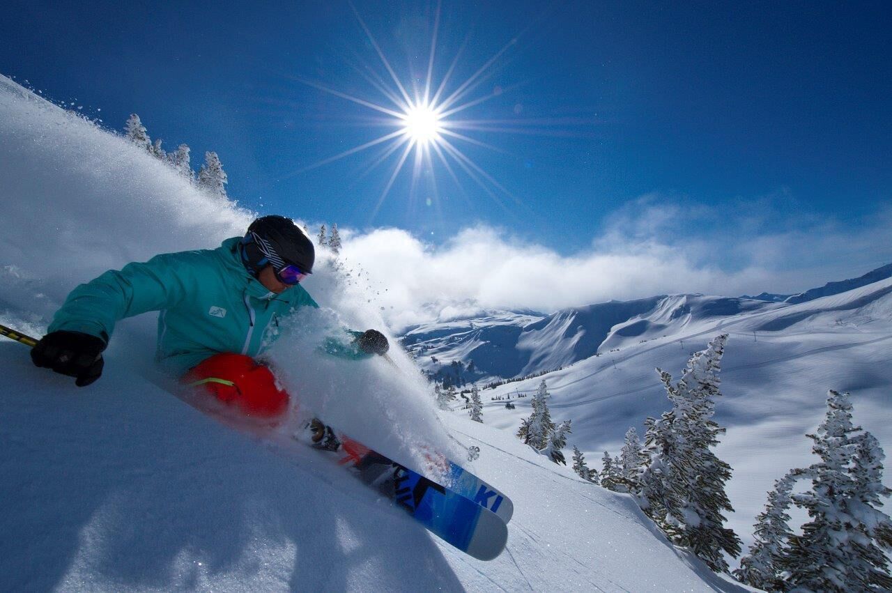 A skier in motion on a snowy slope with a clear sky and sun shining.