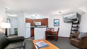 Un espacio habitable compacto con kitchenette, comedor y zona de estar con un televisor montado en la pared.