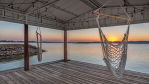 Une terrasse en bois avec un hamac et une vue sur le coucher de soleil sur l’eau.