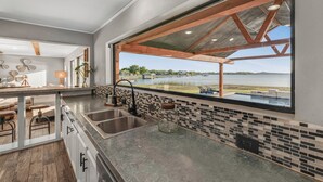 Une cuisine moderne dotée d’une grande fenêtre, offrant une vue sur un lac, et d’un coin repas avec des tabourets de bar.