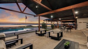 Une terrasse extérieure avec une piscine, un espace salon et une vue sur l’océan au coucher du soleil.