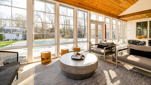 Un salon spacieux avec de grandes fenêtres, une table basse ronde et une vue sur le jardin.