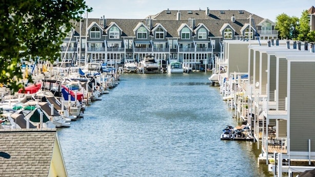 Un port de plaisance où les bateaux sont amarrés le long d’un canal étroit, entouré d’immeubles à plusieurs étages dotés de grandes fenêtres et de balcons.