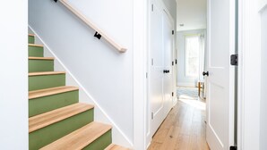 Un escalier avec des marches en bois et des contremarches vertes, menant à un couloir avec des portes blanches et un plancher en bois.