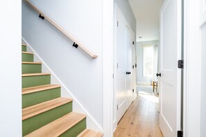A staircase with wooden steps and green risers, leading to a hallway with white doors and a wooden floor.