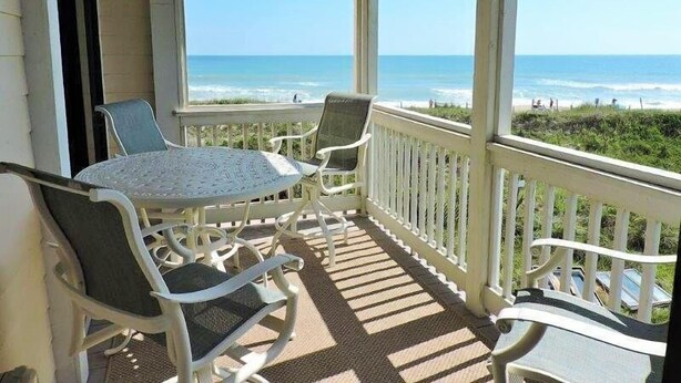 A covered outdoor area with a table and chairs, overlooking the ocean.