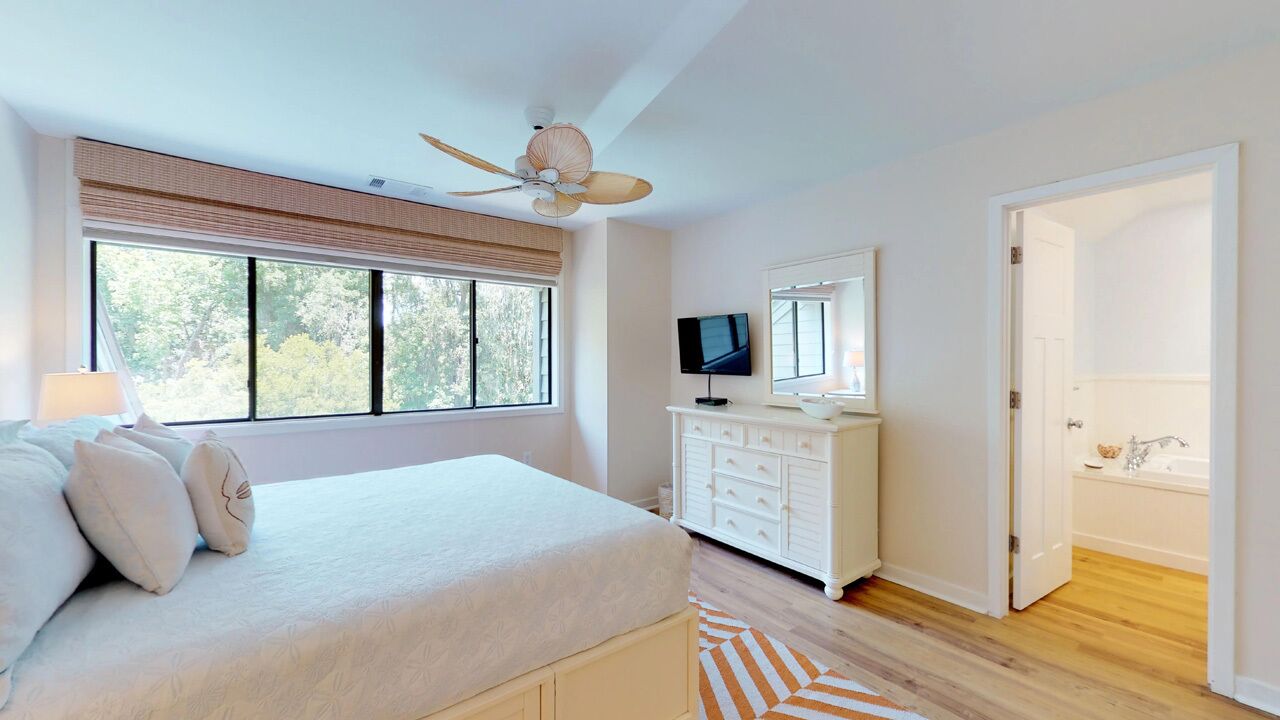 A bedroom with a bed, a TV, a dresser, and a bathroom door.
