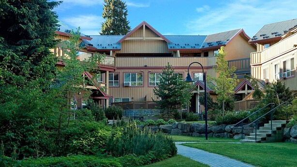 Un chalet doté d’un bâtiment central, entouré d’une végétation luxuriante et accessible par un sentier en pierre.