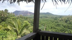 A wooden deck with a view of a lush green landscape and a mountain in the distance. - Castle Tree House (Tanna Island)