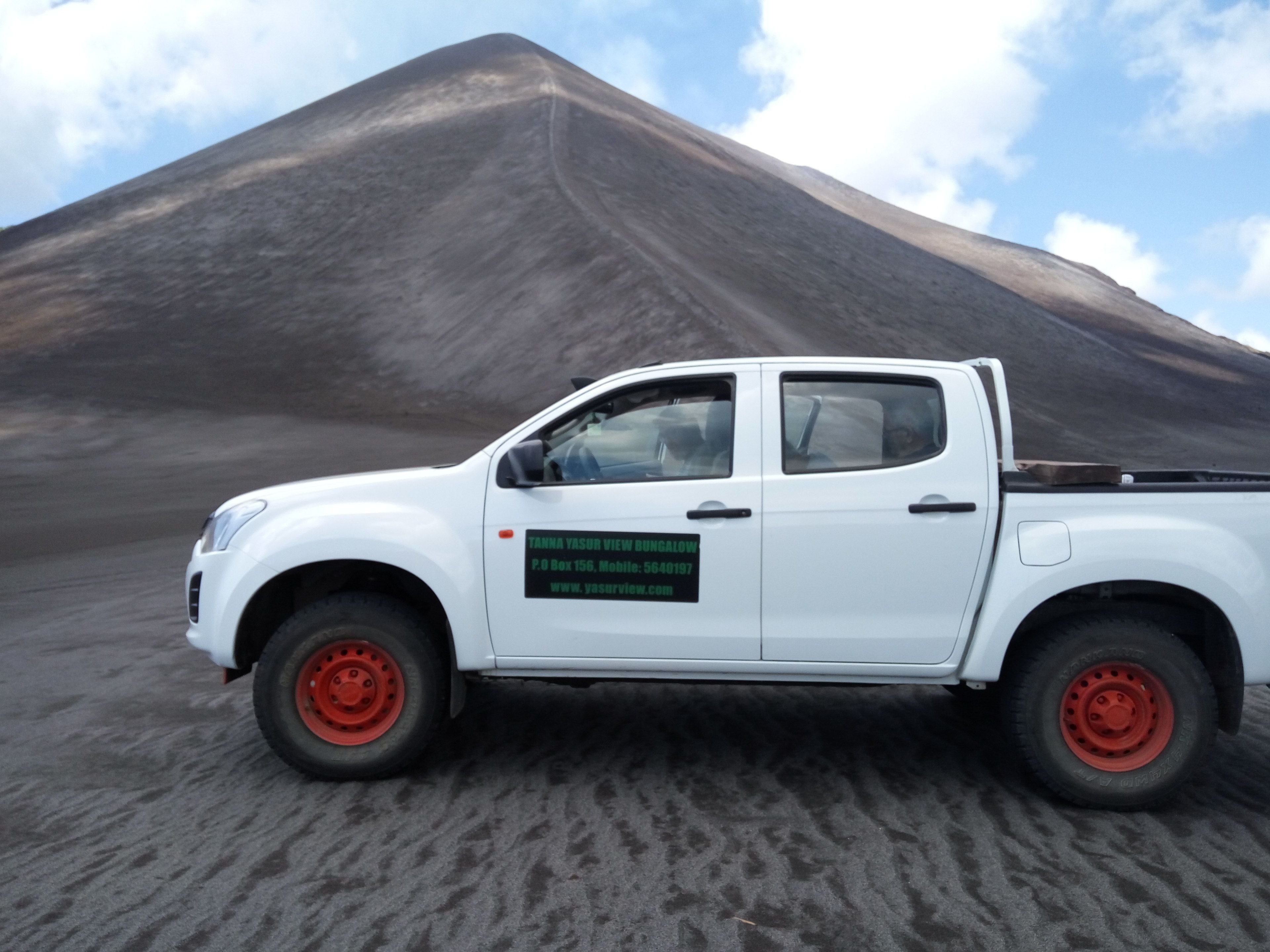 Una camioneta pickup blanca con ruedas rojas estacionada frente a una gran montaña oscura.