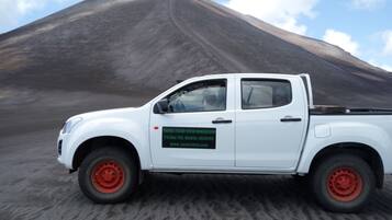 Una camioneta pickup blanca con ruedas rojas estacionada frente a una gran montaña oscura.