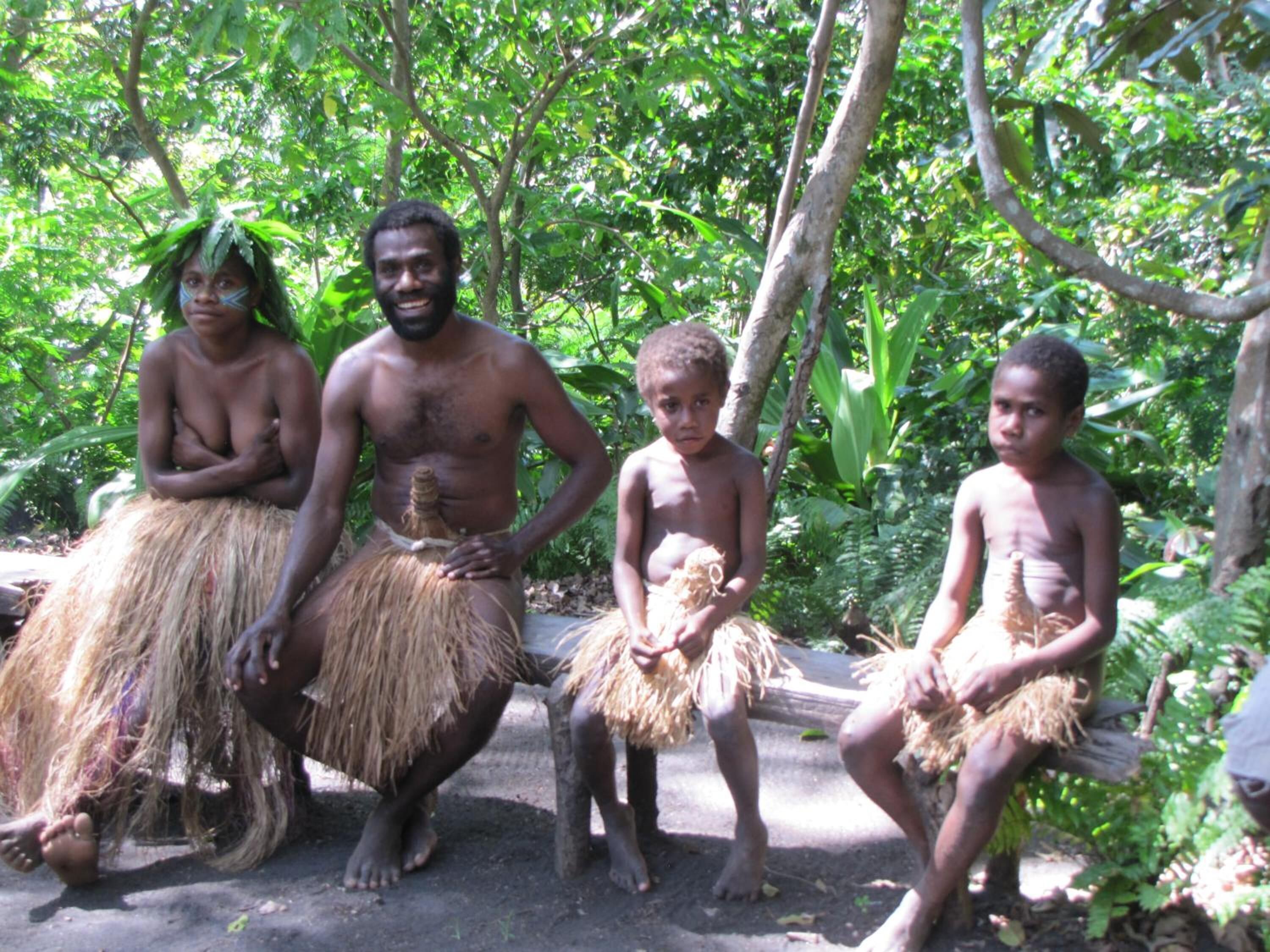 Un groupe de personnes est assis à l’extérieur, dans un cadre naturel, avec un feuillage dense en arrière-plan.
