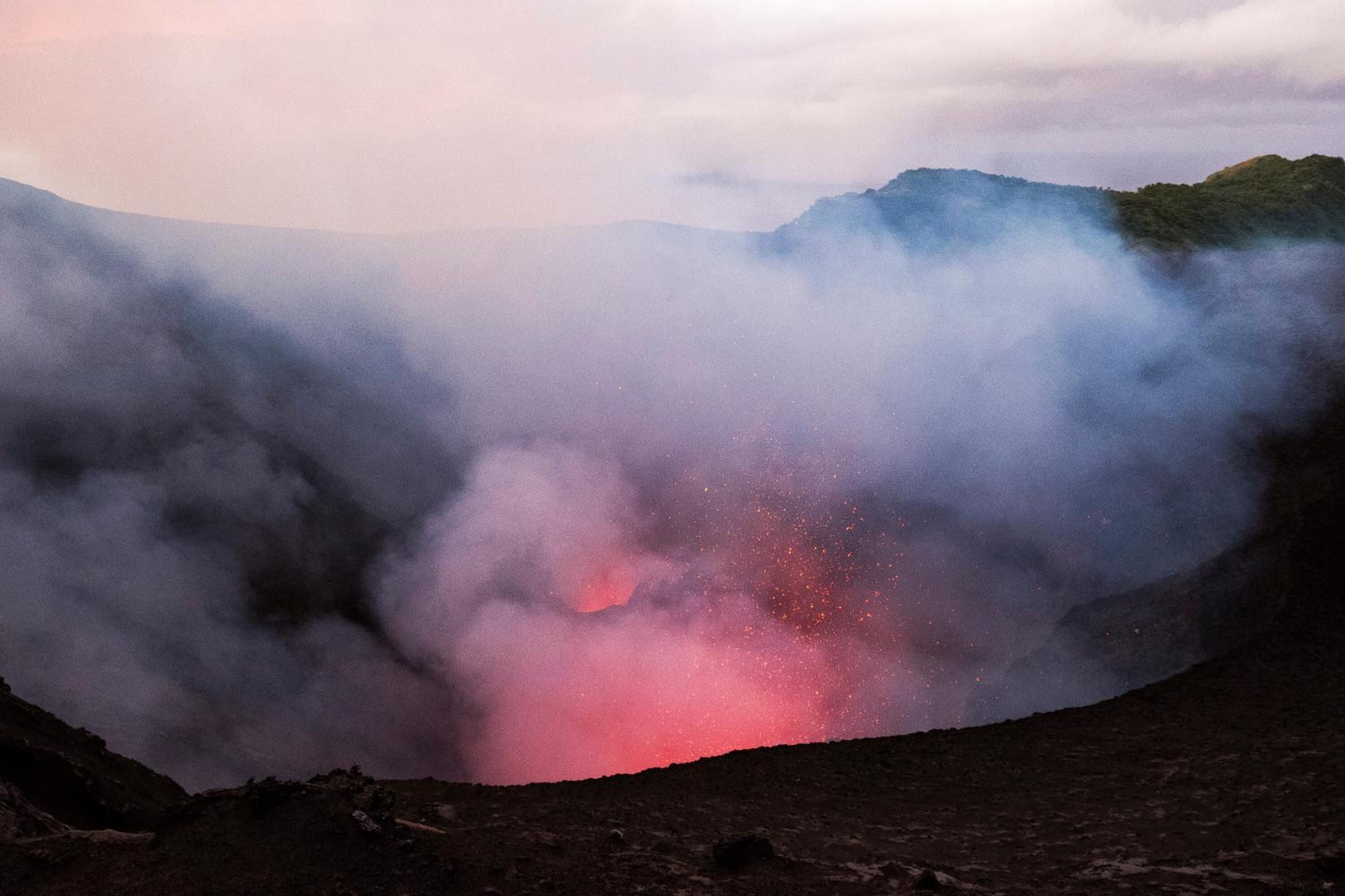 A volcanic landscape with a glowing lava flow and smoke rising from the crater.