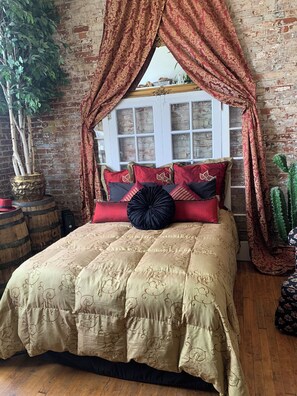 A bed with a gold and red patterned bedspread, red and black pillows, and a black decorative pillow.