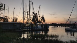 Un port de plaisance où sont amarrés de nombreux bateaux, une jetée qui s’avance dans l’eau et un coucher de soleil en arrière-plan.