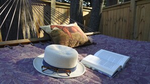 Un hamac, un chapeau et un livre ouvert, posés sur un tissu à motifs.