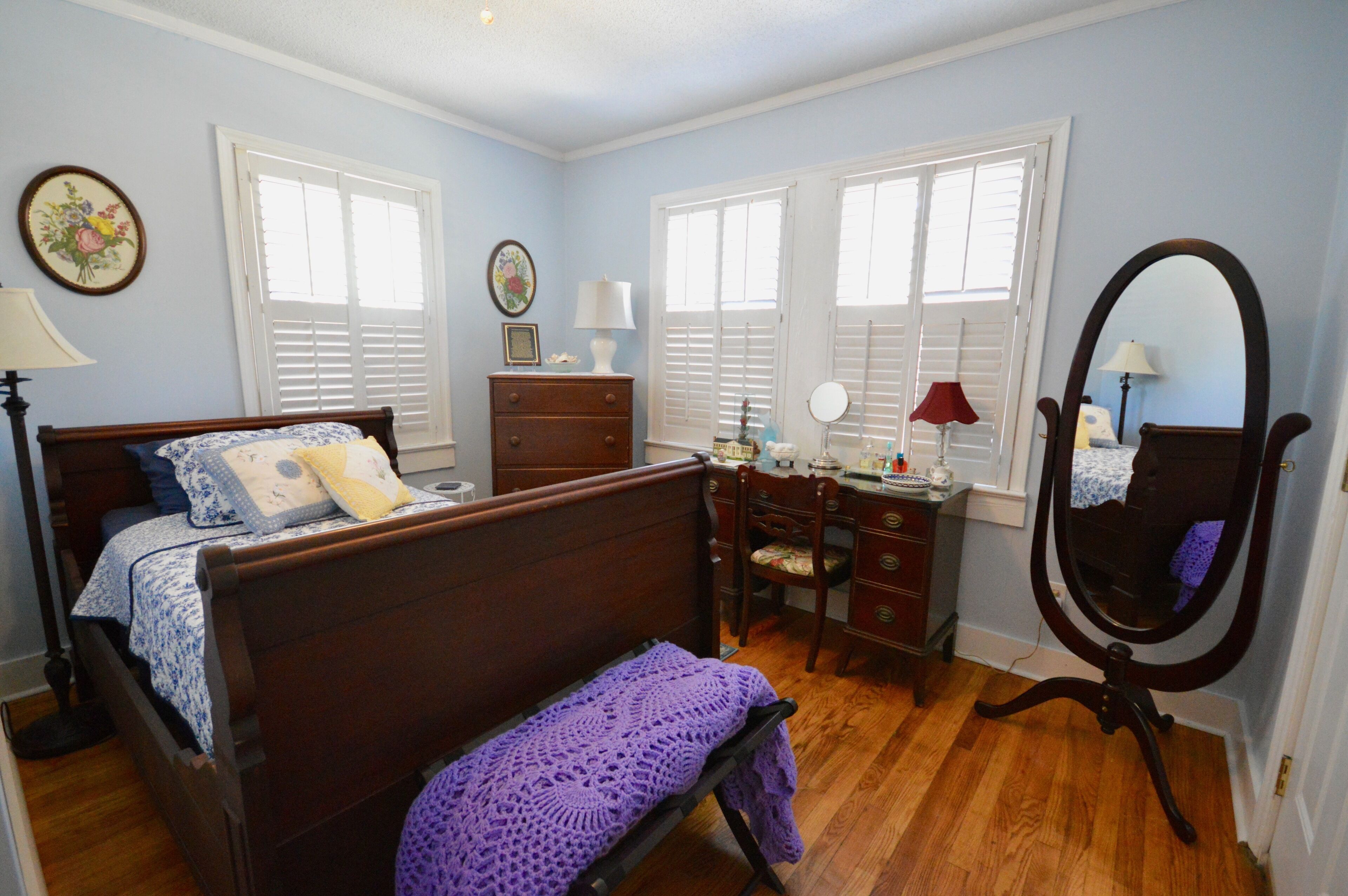 Quarto com cama de madeira, cômoda, escrivaninha com espelho e janela com persianas.