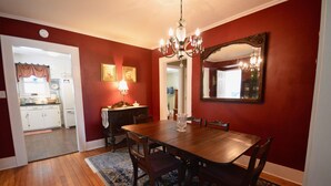 Une salle à manger avec une table en bois, des chaises, un lustre et un grand miroir au mur.