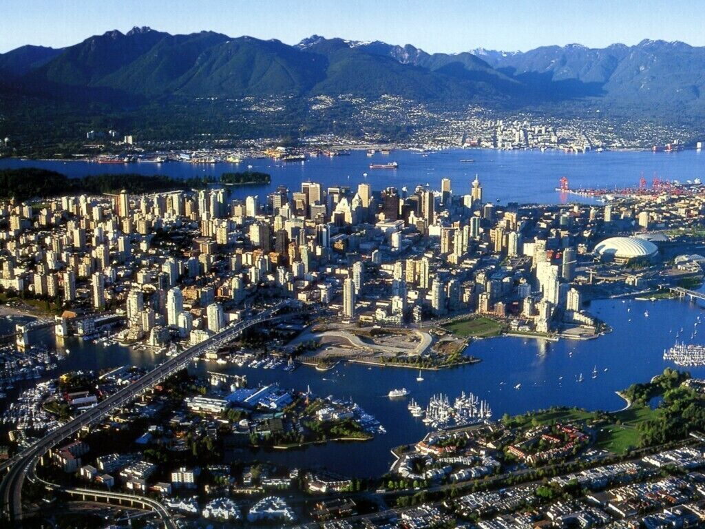 A cityscape with a dense cluster of high-rise buildings, a marina with boats, and a large stadium.