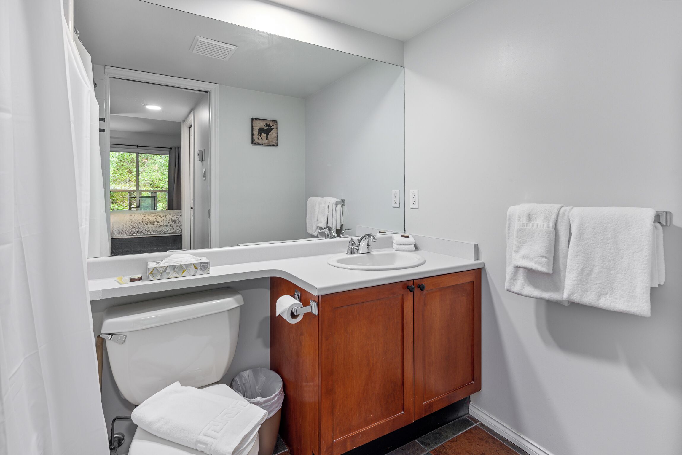 A modern bathroom with a white sink, wooden vanity, and a large mirror.