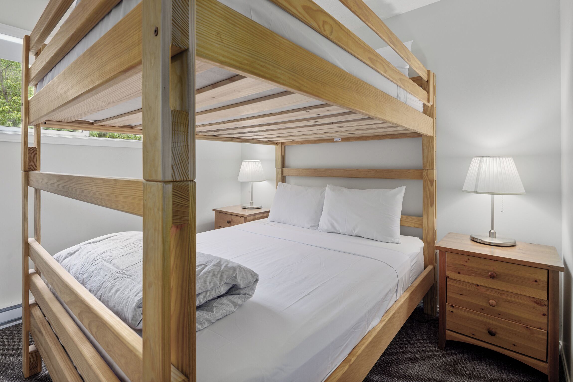 Un lit superposé avec une structure en bois, une literie blanche et deux tables de chevet avec des lampes.
