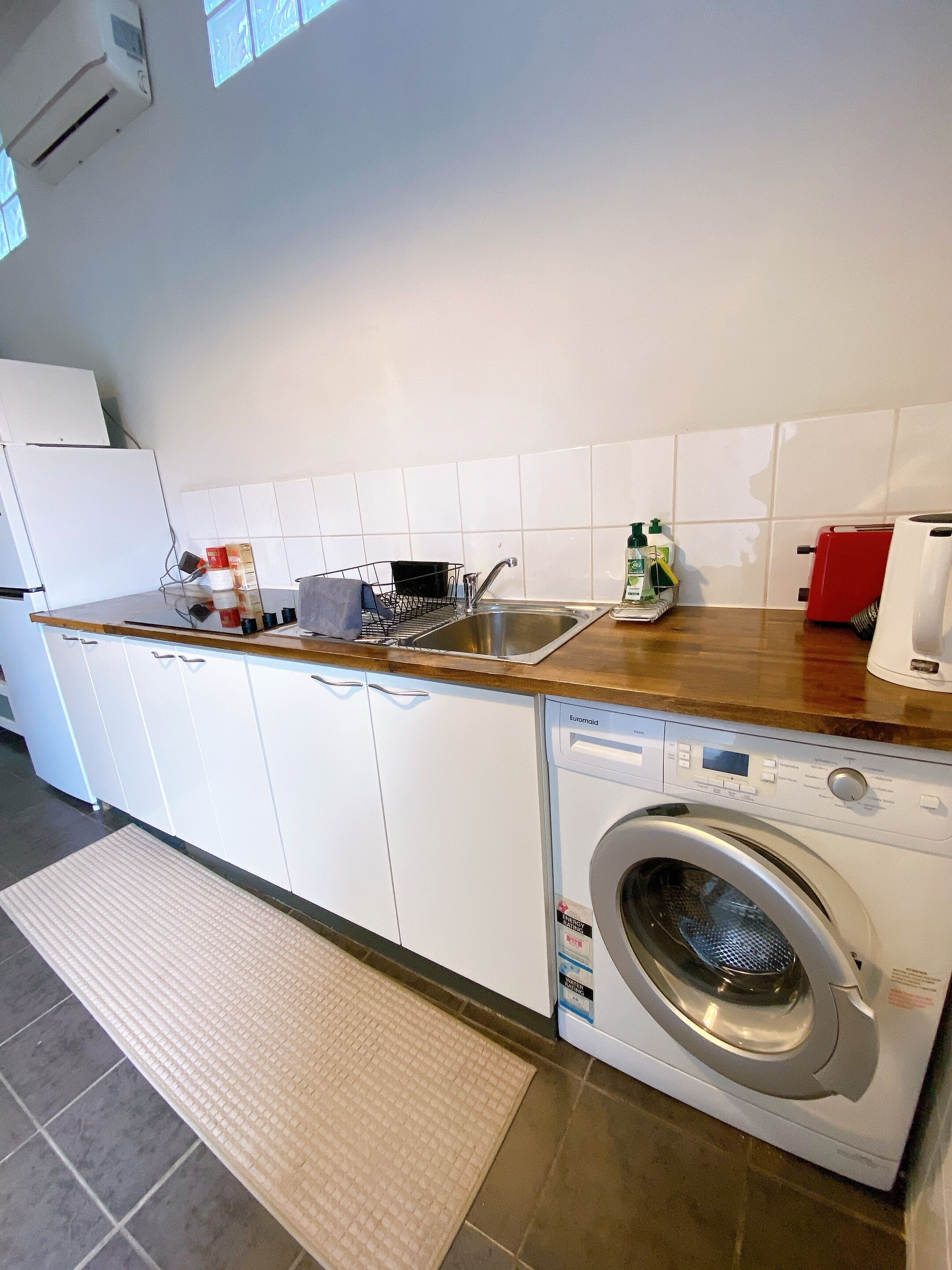 Une cuisine compacte équipée d’un lave-linge intégré, d’un évier et d’un plan de travail sur lequel sont disposés divers objets.