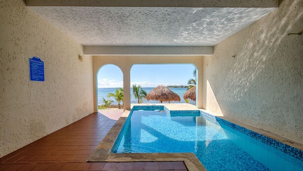 A pool area with a view of the ocean, a thatched umbrella, and a sign on the wall. - Amazing View Oceanfront with 2 pools, Daily Housekeeping (Akumal)