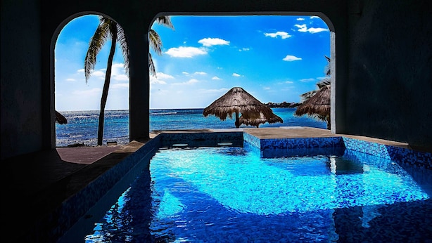 Ein Pool mit klarem, blauem Wasser, Blick auf den Ozean und Palmen.