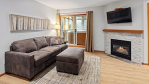 Ein Wohnzimmer mit einer Couch, Hocker, Kamin, Fernseher und Kunstwerken an der Wand.