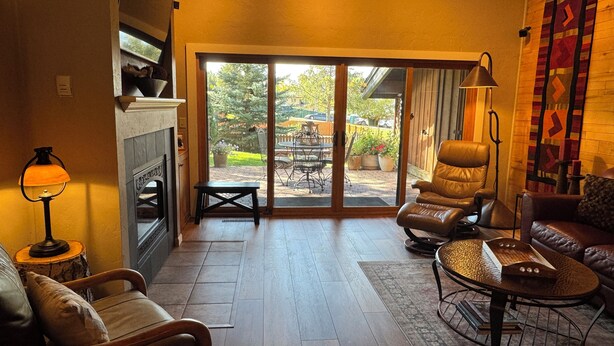 A cozy living room with a fireplace, leather chairs, a coffee table, and a view through large sliding glass doors to an outdoor patio. - Make Memories - Just Steps to the Shuttle, Close to Base, and Locker at the Base (Steamboat Springs)