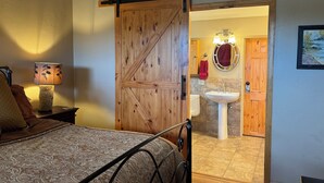 A bedroom with a bed, a nightstand with a lamp, a wooden wardrobe, and a sliding door leading to a bathroom with a sink and toilet. - Make Memories - Just Steps to the Shuttle, Close to Base, and Locker at the Base (Steamboat Springs)