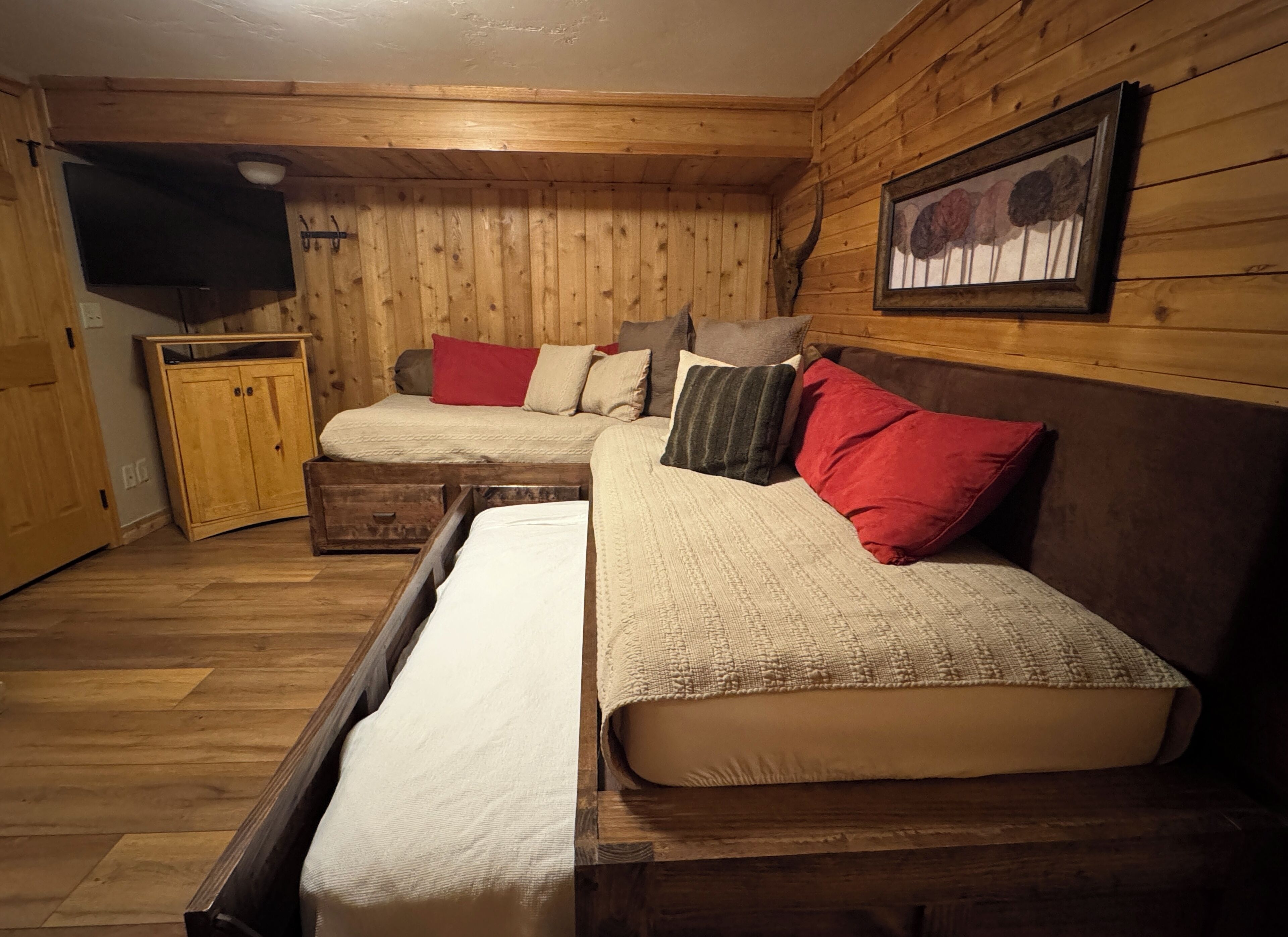 Una habitación acogedora con paredes de madera, una cama con muchos cojines, un banco y un televisor en la pared.