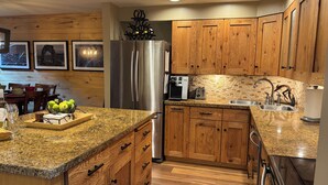 A kitchen with wooden cabinets, granite countertops, a stainless steel refrigerator, a coffee maker, and a toaster. - Make Memories - Just Steps to the Shuttle, Close to Base, and Locker at the Base (Steamboat Springs)