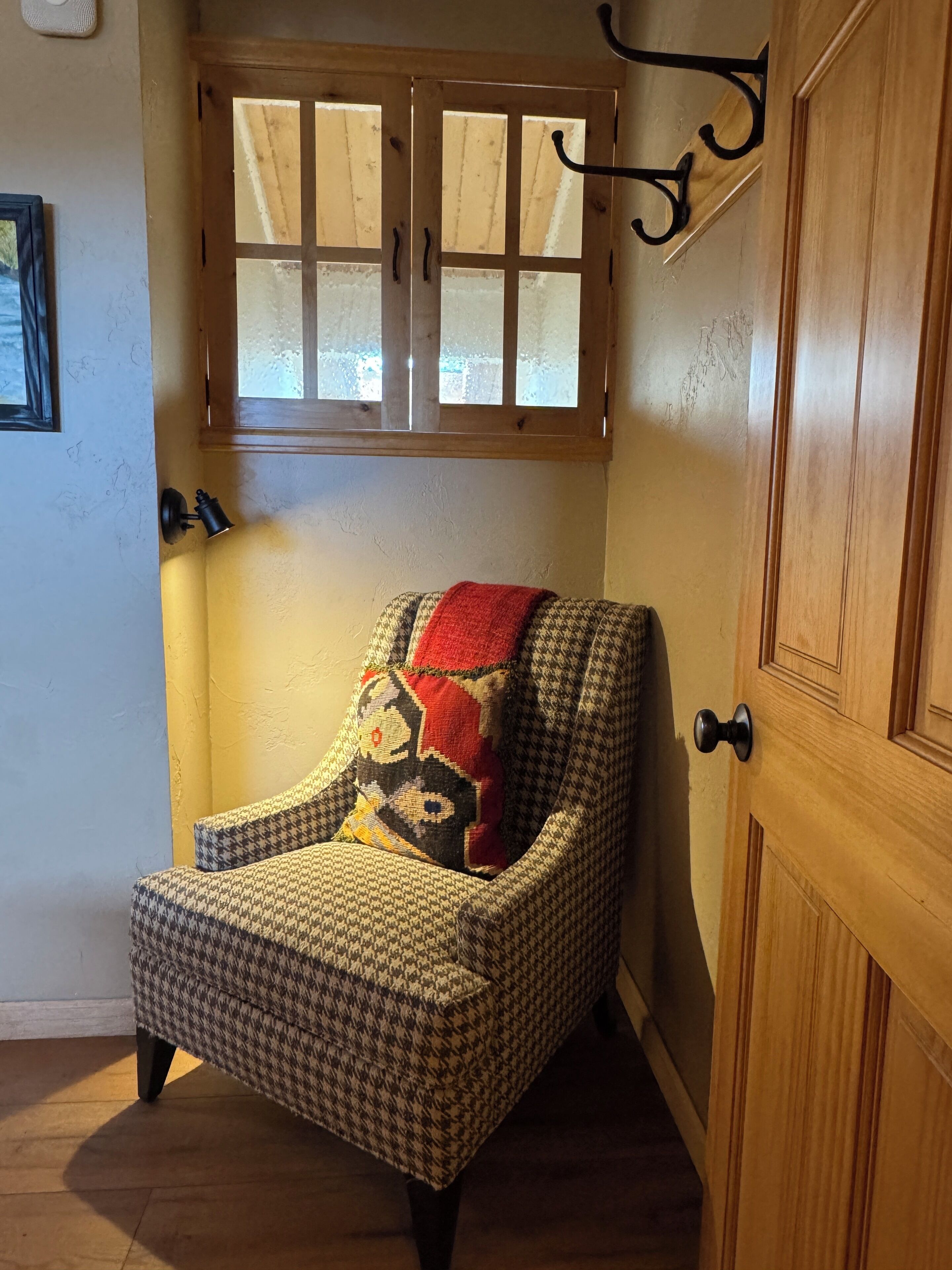 Uma poltrona com padrão xadrez de houndstooth e almofada vermelha e preta, colocada em frente a uma porta de madeira com uma janela acima.