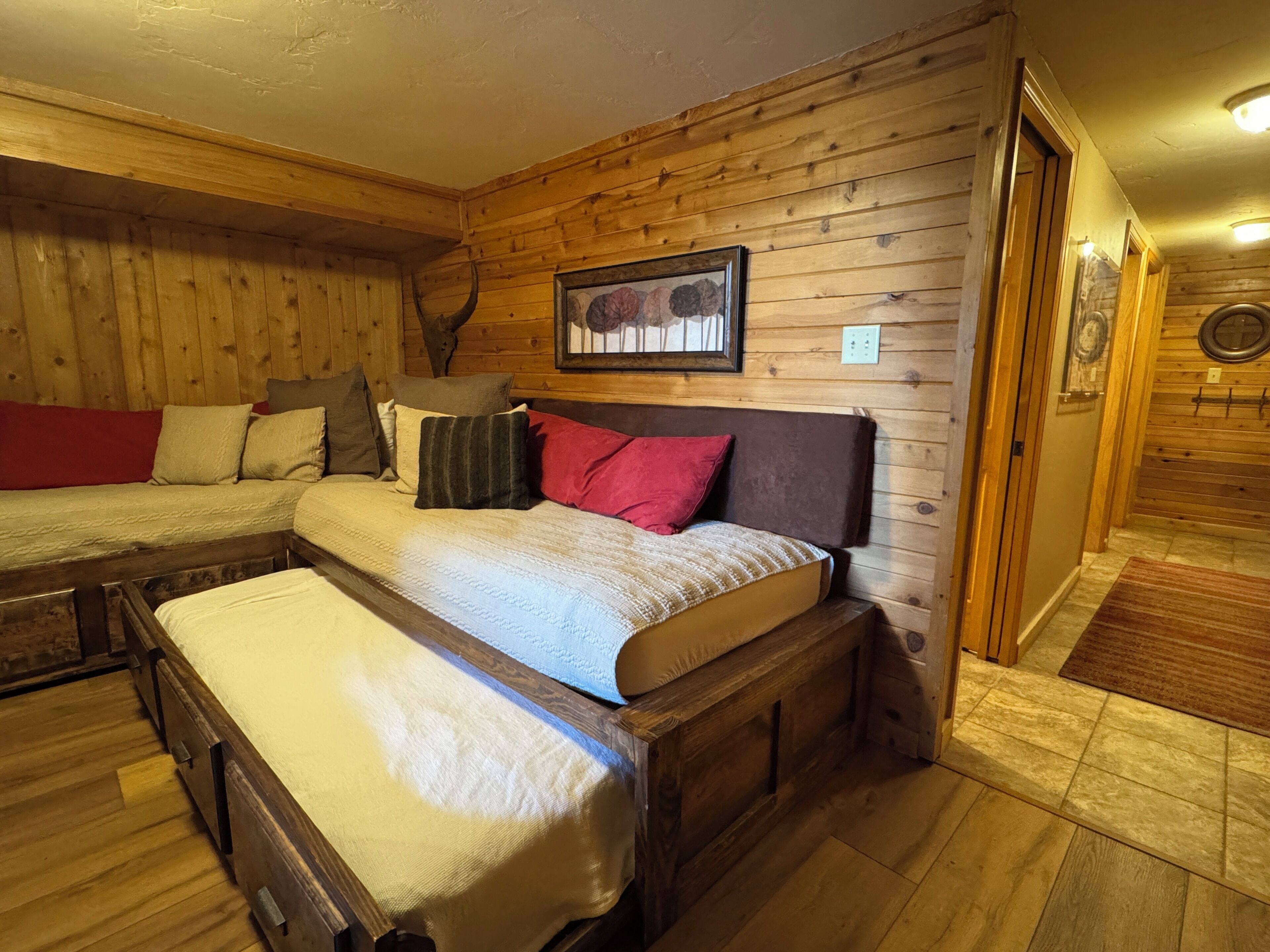 A cozy room with wooden walls and a bed with a headboard. There is a framed picture on the wall and a small rug on the floor.